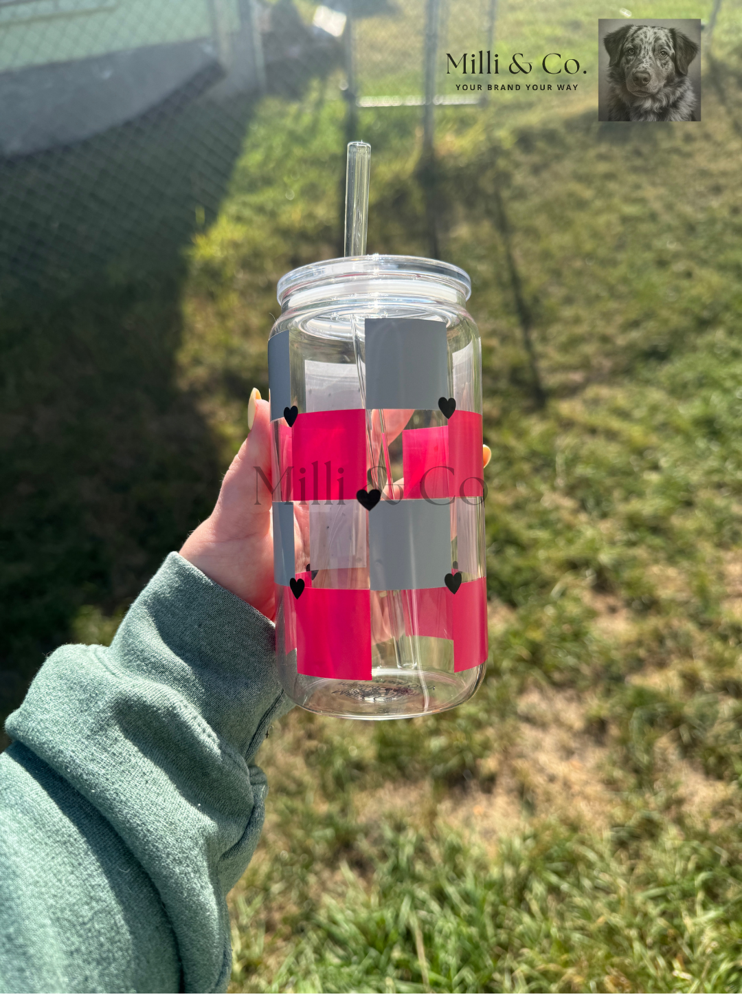 Clear water bottle with pink checkered design held by a person outdoors