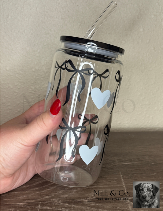 20oz clear glass tumbler with reusable glass straw, black bow and blue heart design, plastic lid, displayed on wooden surface.