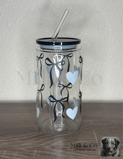 20oz clear glass tumbler with reusable glass straw, black bow and blue heart design, plastic lid, displayed on wooden surface.